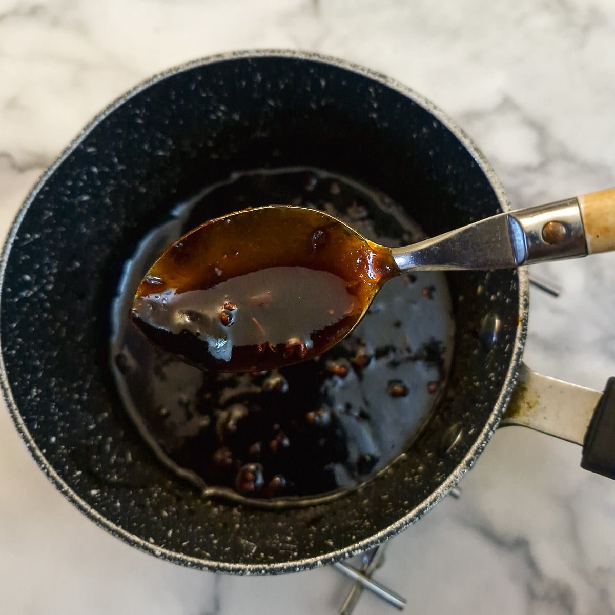 Sticky gochujang sauce in a sauce pan with a spoonful being lifted out to show the consistency.