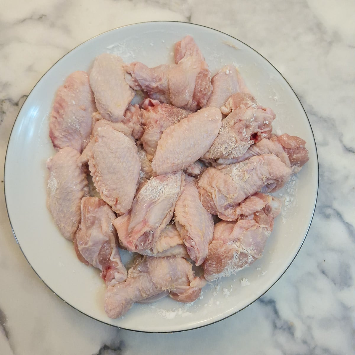 Jointed chicken wings coated with olive oil and cornflour on a white plate.
