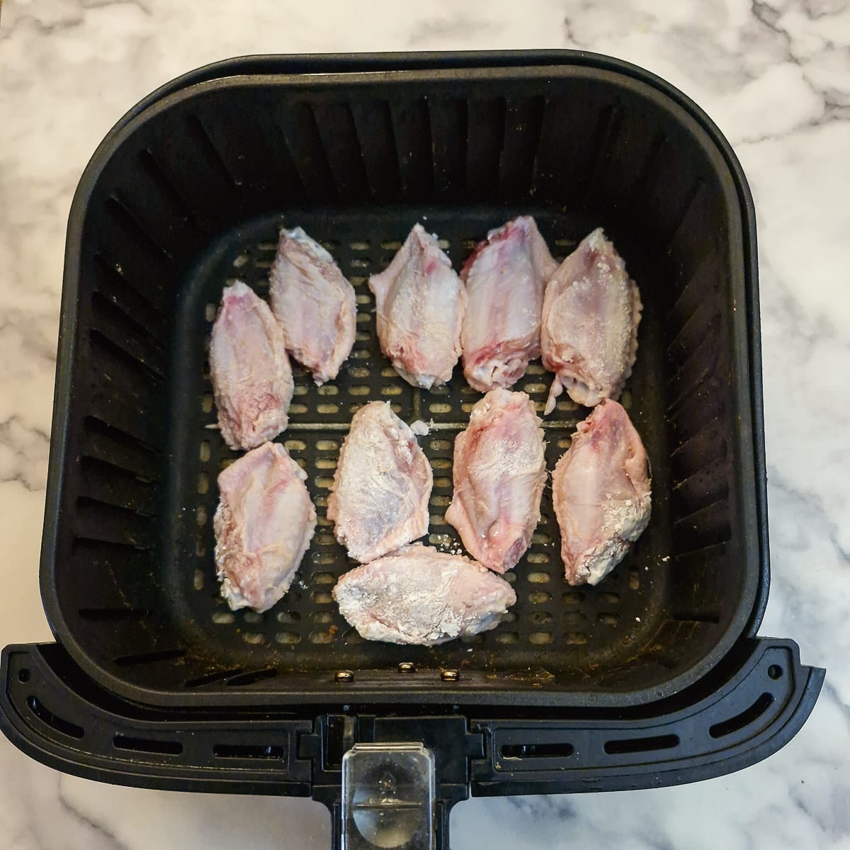 A layer of raw chicken wings in an air-fryer basket.