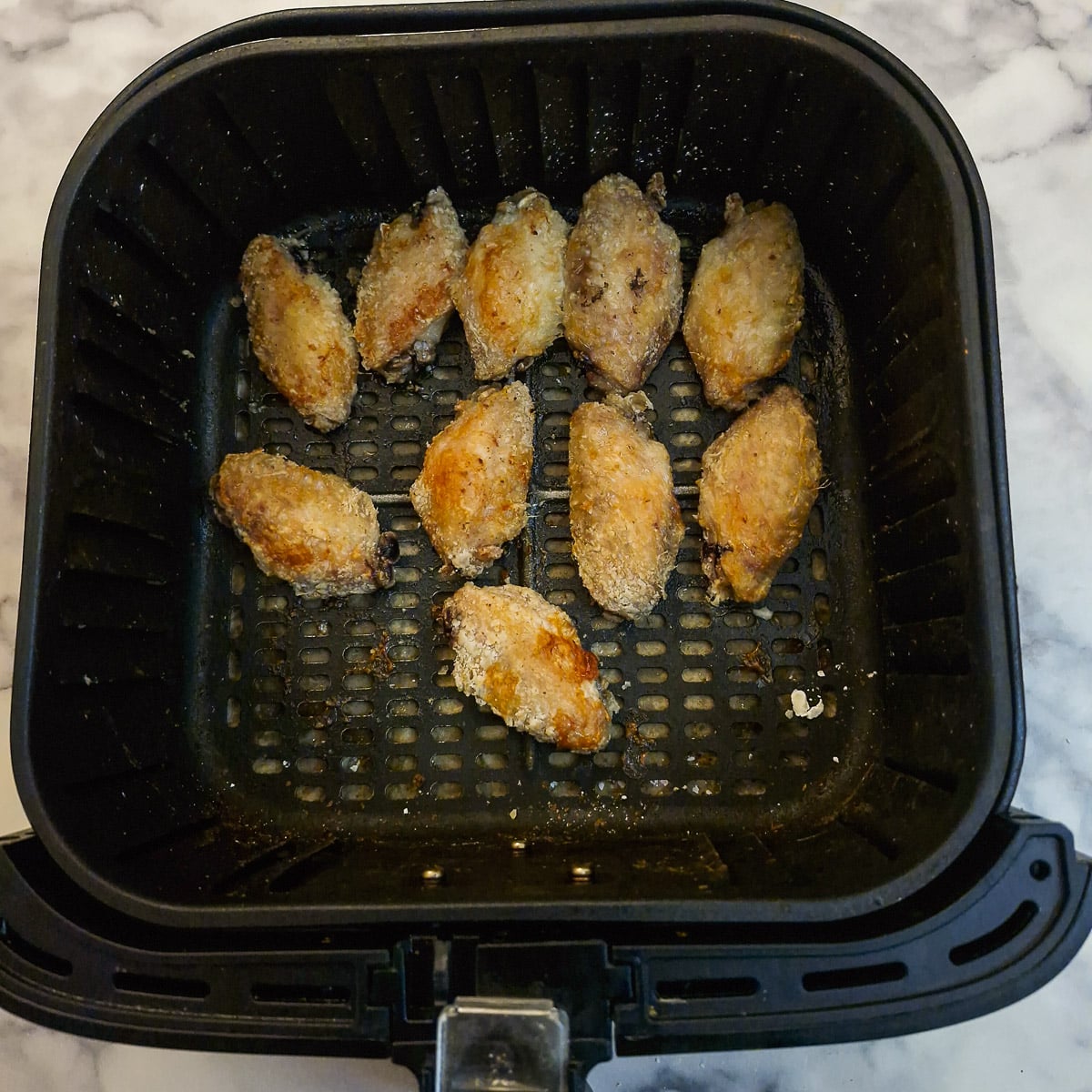 A layer of crispy browned chicken wings in an air-fryer basket.