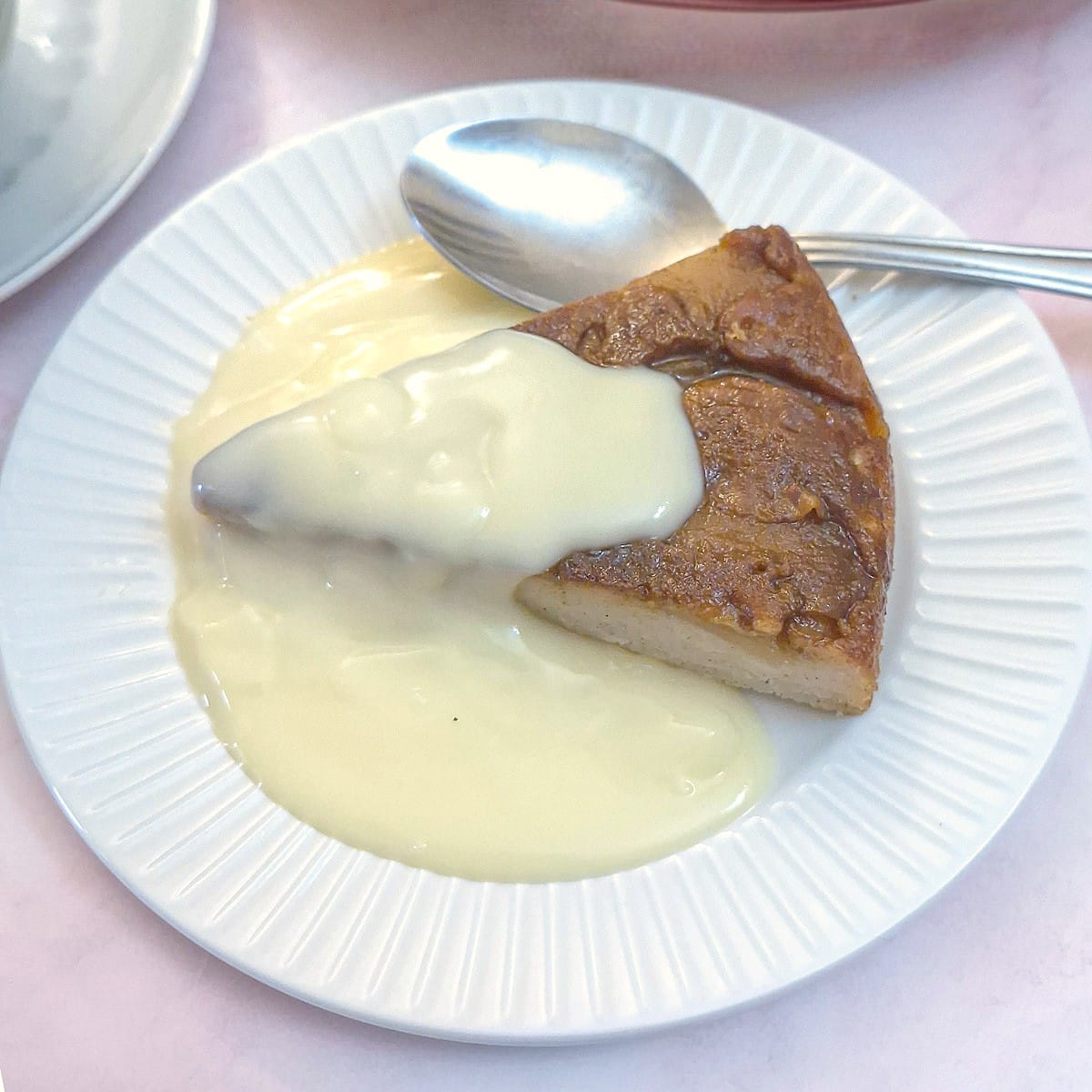A slice of apple frying pan cake on a white serving plate with a serving of custard.