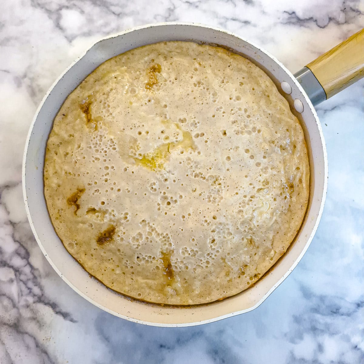 Apartially cooked apple cake in a frying pan. The top of the cake is still slightly damp.