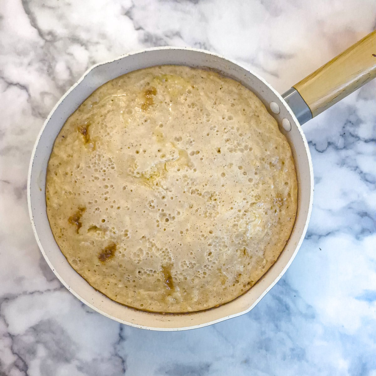A fully cooked frying pan apple cake still in the pan. You can see how the edges of the cake have pulled slightly away from the sides of the pan as it has cooled.