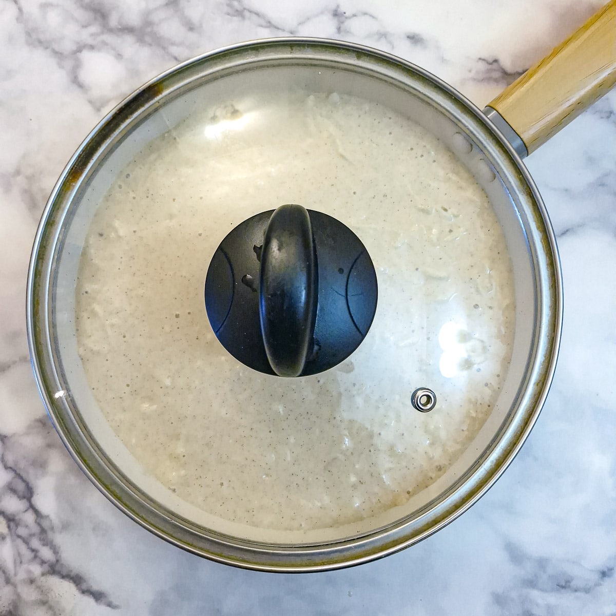 The unbaked apple cake in a frying pan, covered with a glass lid.