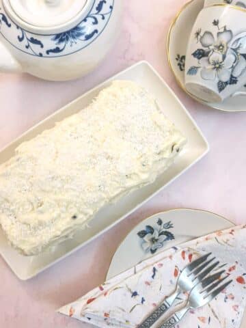 Overhead sh;ot of a granadilla coconut loaf cake on a teatable with teacups and a teapot.