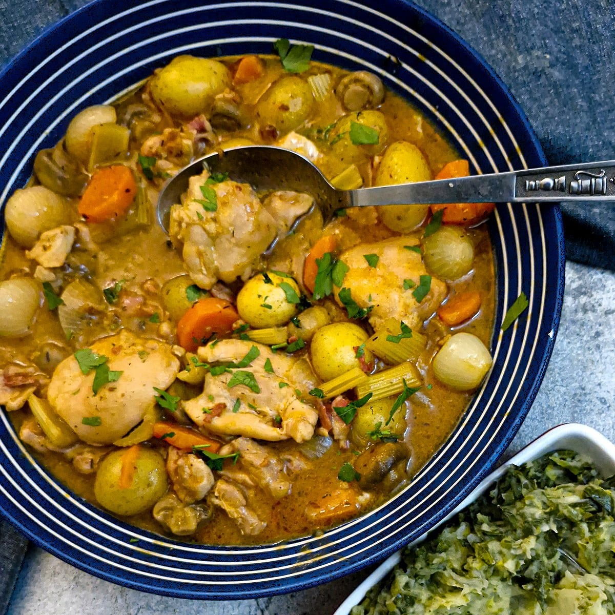 A blue and white rimmed large serving dish filled with chicken cider casserole. There is a dish of spring green mash in the foreground.