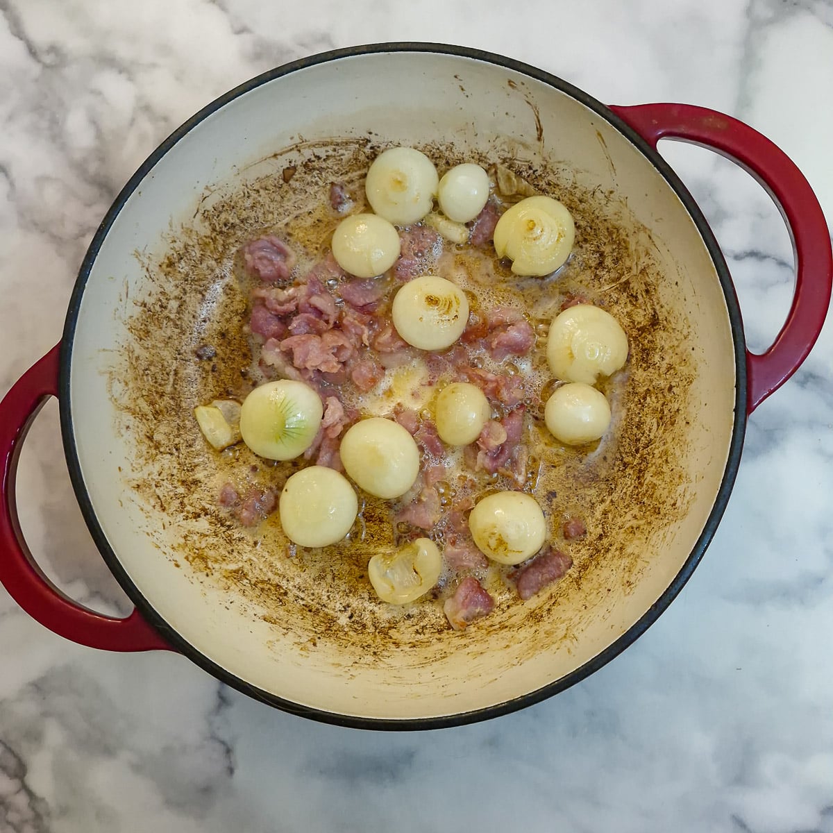 Bacon and pearl onions browning in a casserole dish.