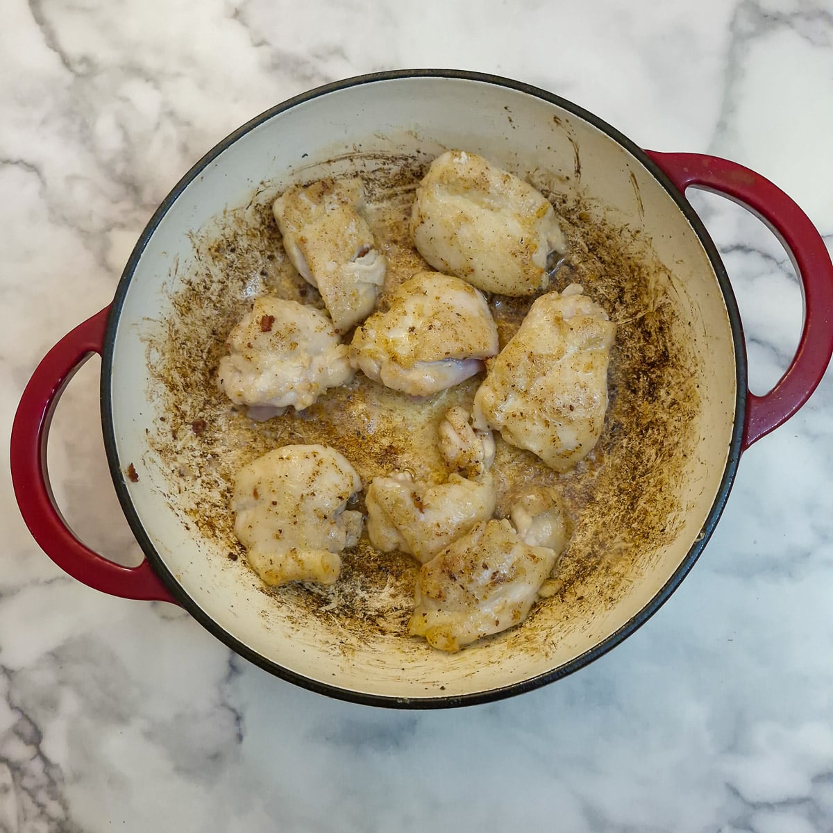 Pieces of chicken thigh fillet browning in a casserole dish.