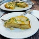 A slice of welsh onion potato cakeon a white plate with a fork. There is the entire cake in the background.