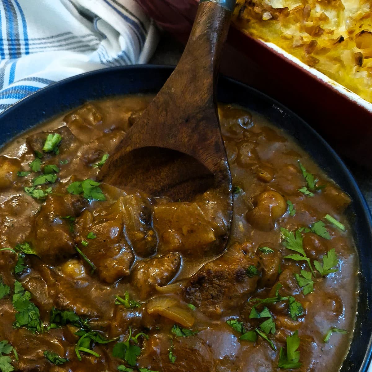 Closeup of the beef and mushroom stew showing a wooden spoon holding pieces of beef in thick gravy.