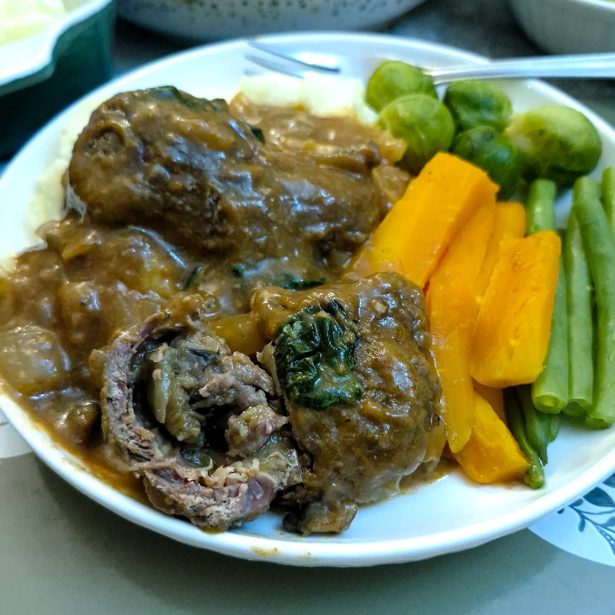 Two beel olives on a white plate. One beef olive has been cut in half to show the mushroom filling on the inside.