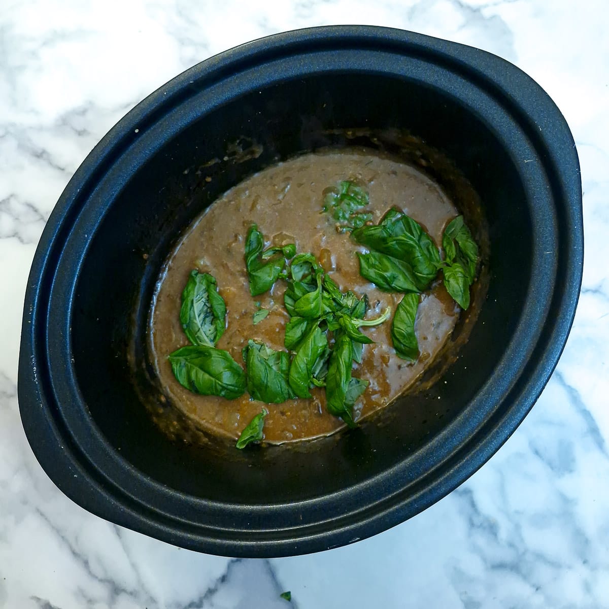 Step 12 - gravy that has been thickened in a slow cooker. Pieces of fresh basil have been stirred in to wilt.