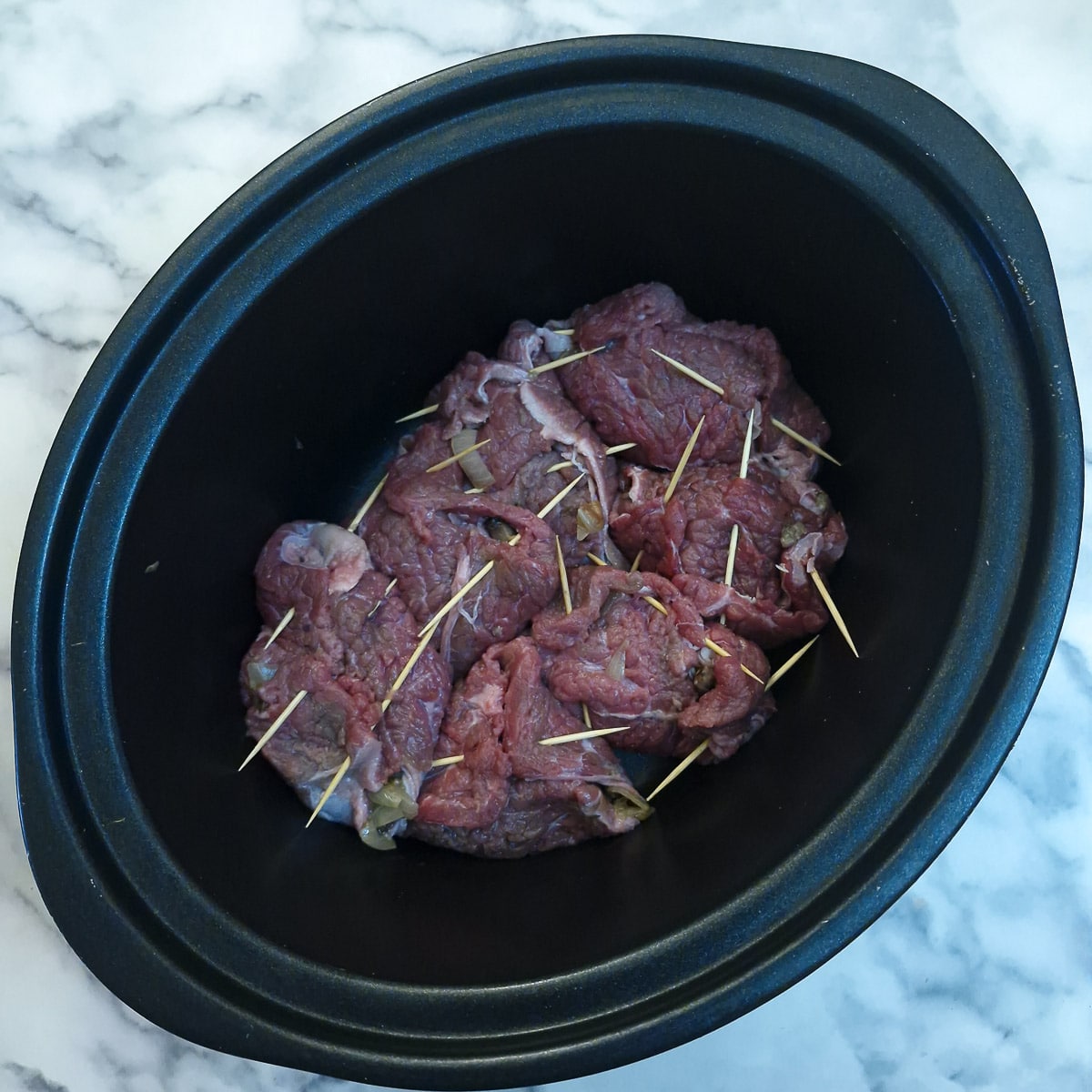 Step 8 - beef rolls secured with toothpicks arranged in a slow cooker.