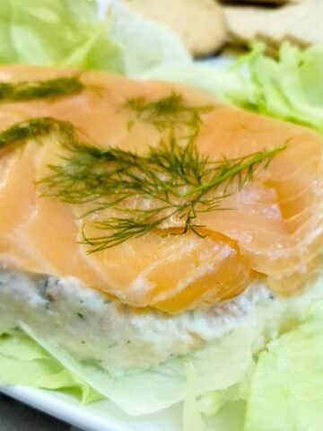 Salmon and dill terrine on a bed of lettuce on a white plate. There are fresh sprigs of dill on top.