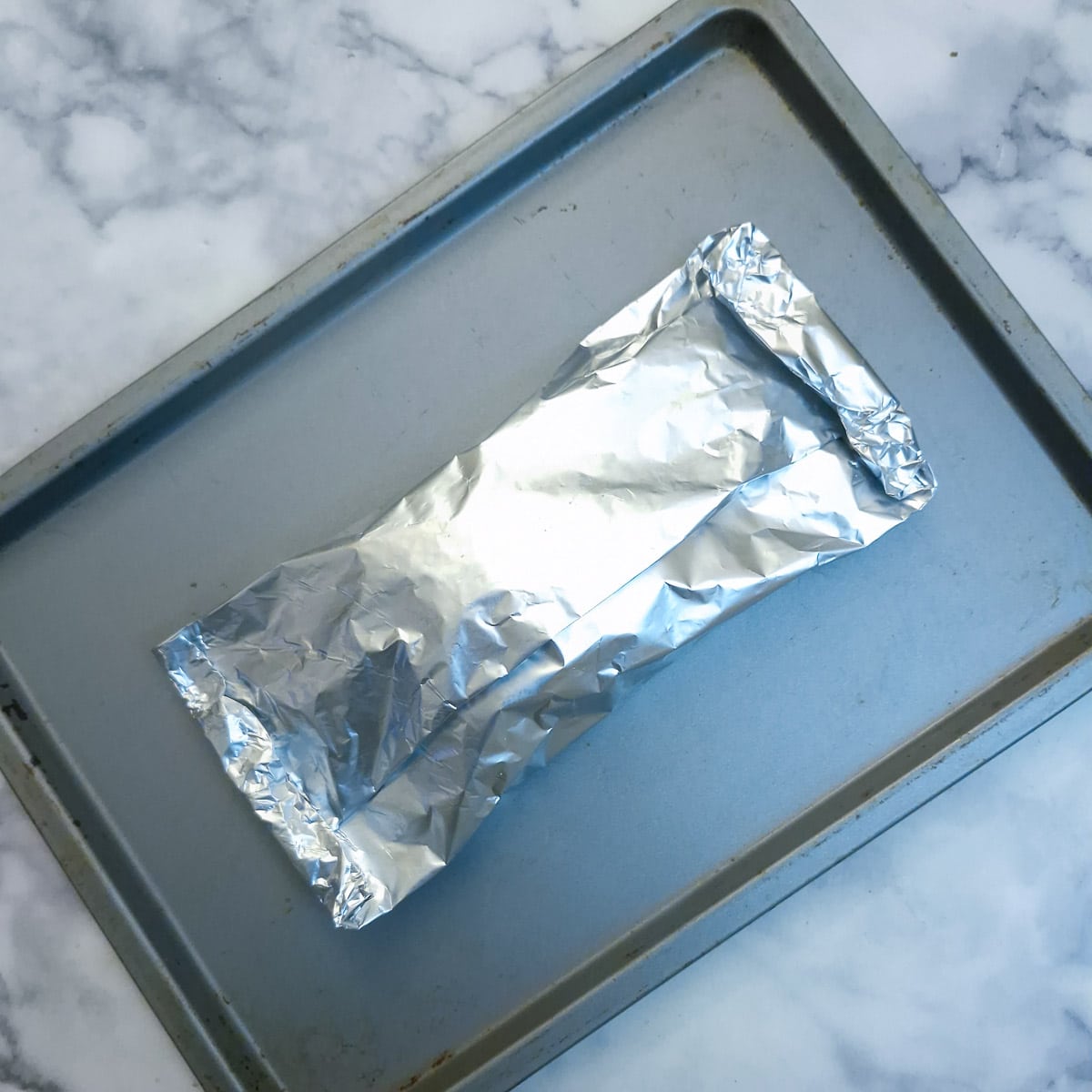 A foil-wrapped parcel of salmon ready to go into the oven on a baking tray.