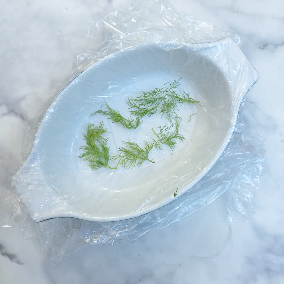 A small white dish, lined with clingfilm with a few sprigs of fresh dill on the bottom.