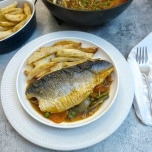 A piece of crispy-skinned sea bass on a dish of garlic vegetable sauce with french fries on the side.