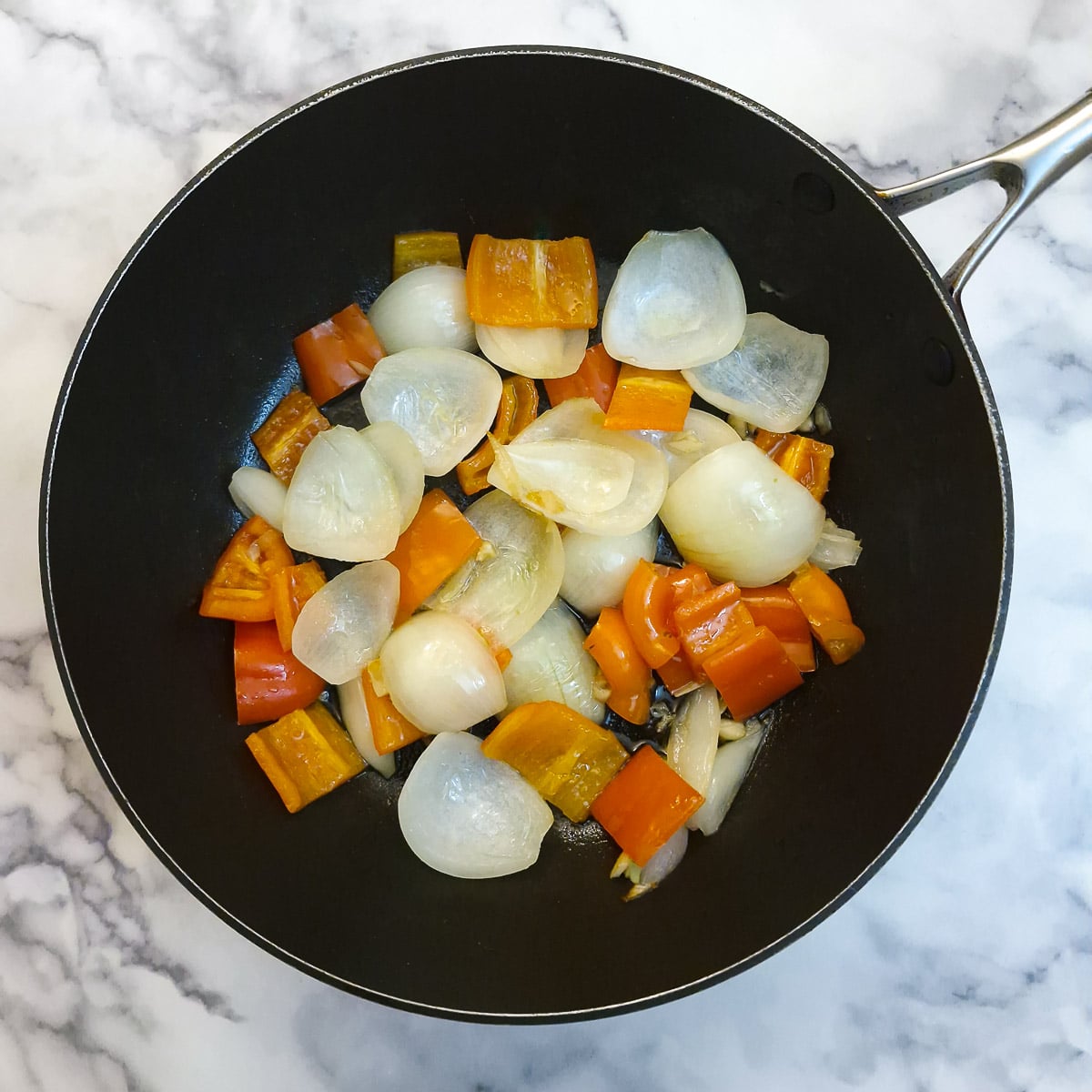 Onions and red peppers softening in a frying pan.