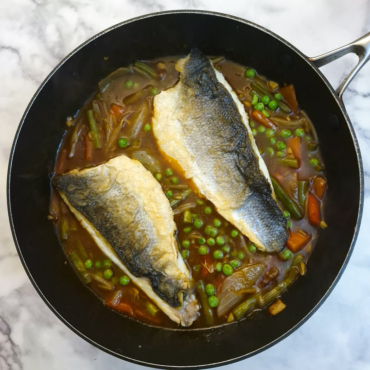 Two sea bass fillets arranged skin side up on top of the sauce.