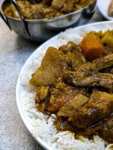 Close up of a plate on lamb curry on a bed of white rice.