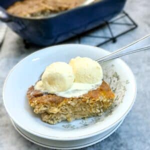 A serving of Biscoff apple pudding cake in a small white dessert bowl, topped with a scoop of ice cream.