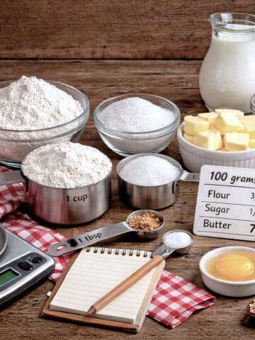 Baking ingredients in dishes on a table. There is a kitchen scale and a few measuring spoons alongside.