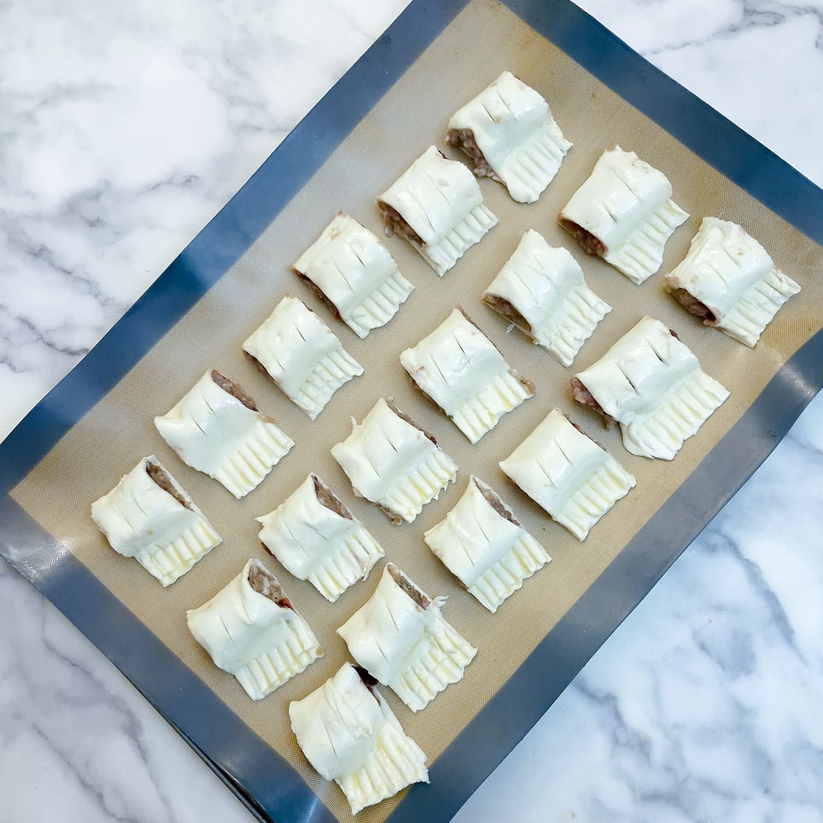 18 mini sausage rolls on a silicone-lined baking tray.