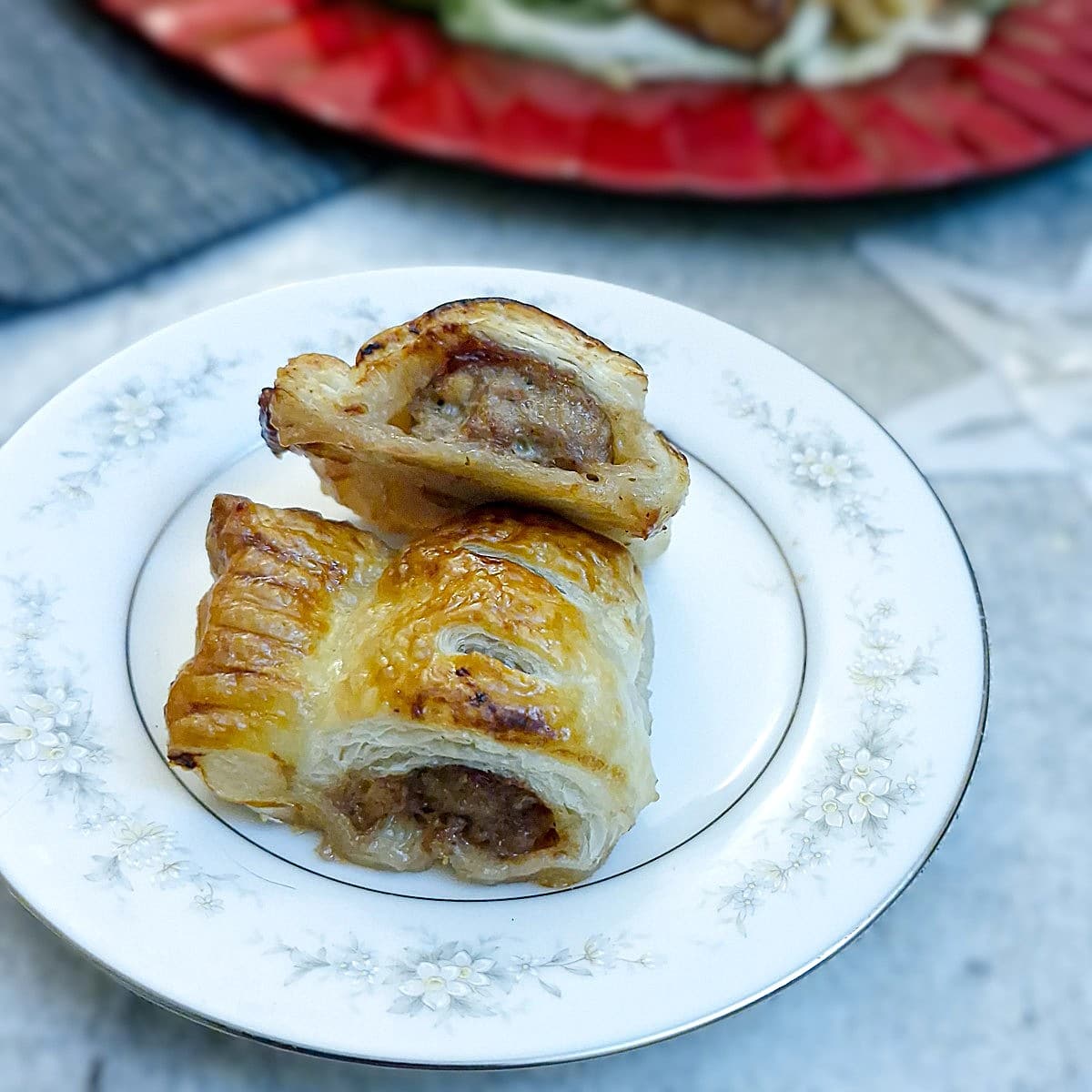 Close-up of 2 leftover cranberry sauce sausage rolls on a blue-patterened plate.