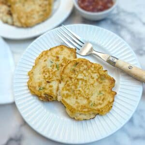 2 potato cakes on a white plate with a fork on the side.