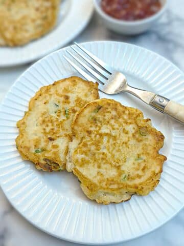 2 potato cakes on a white plate with a fork on the side.