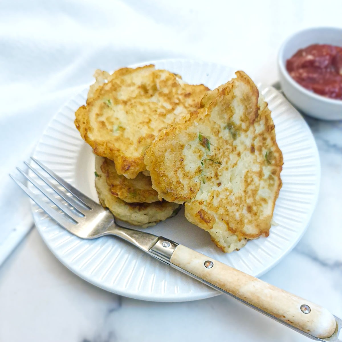 A pile of potato cakes on a small white plate with one potato cake resting against the side of the pile.
