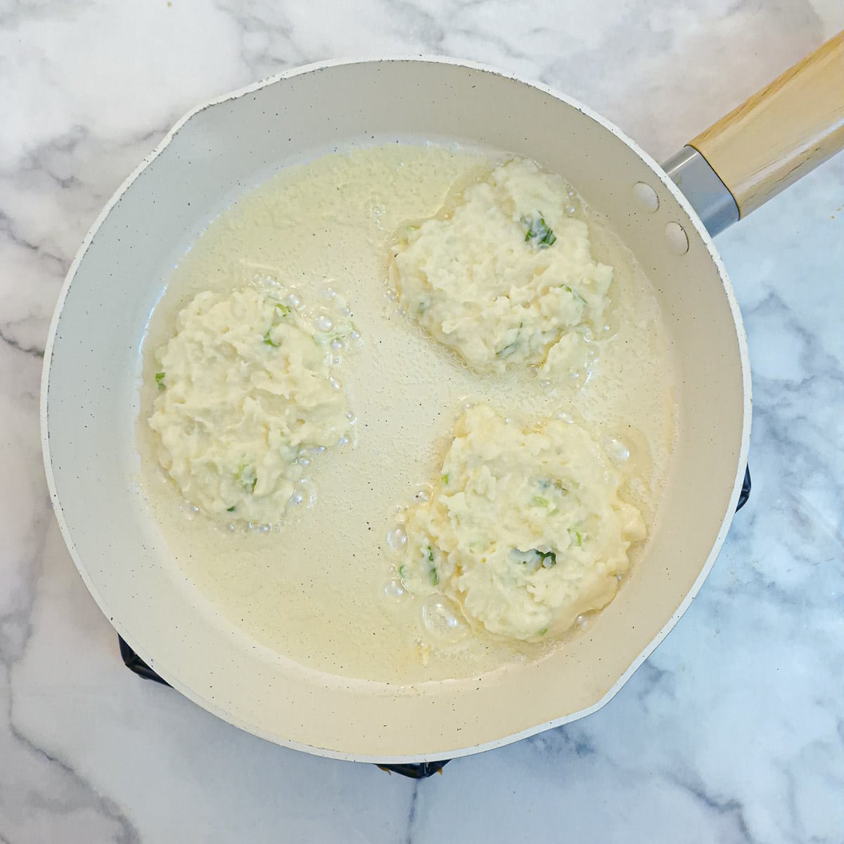 Step 4 - 3 potato cakes browning in a frying pan.