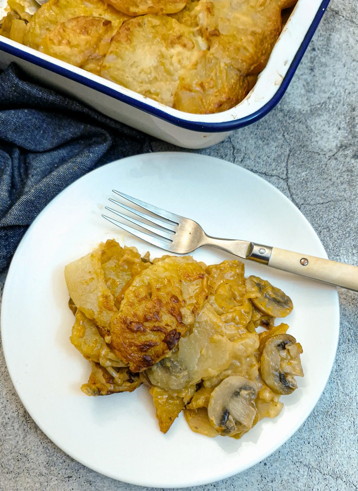 A serving of potatoes Diane on a small white plate, showing the layers of potatoes and mushrooms. There is a fork on the plate.