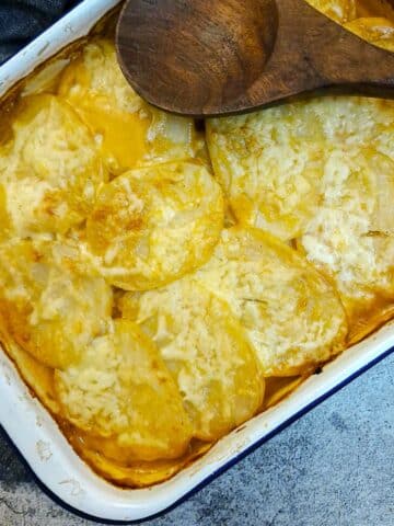 Overhead shot of a dish of potatoes Diane with a large wooden serving spoon resting on the dish.
