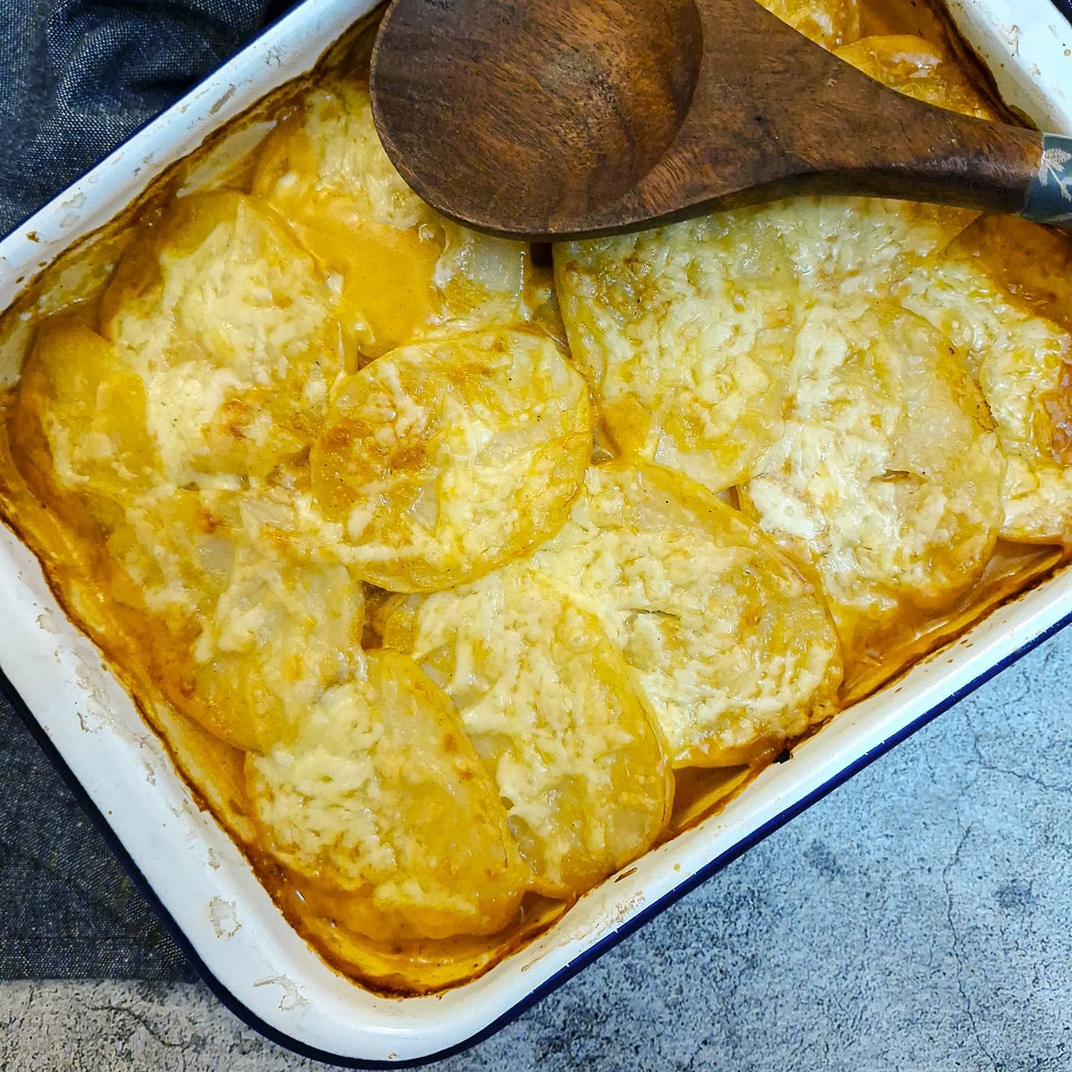 Overhead shot of a dish of potatoes Diane with a large wooden serving spoon resting on the dish.