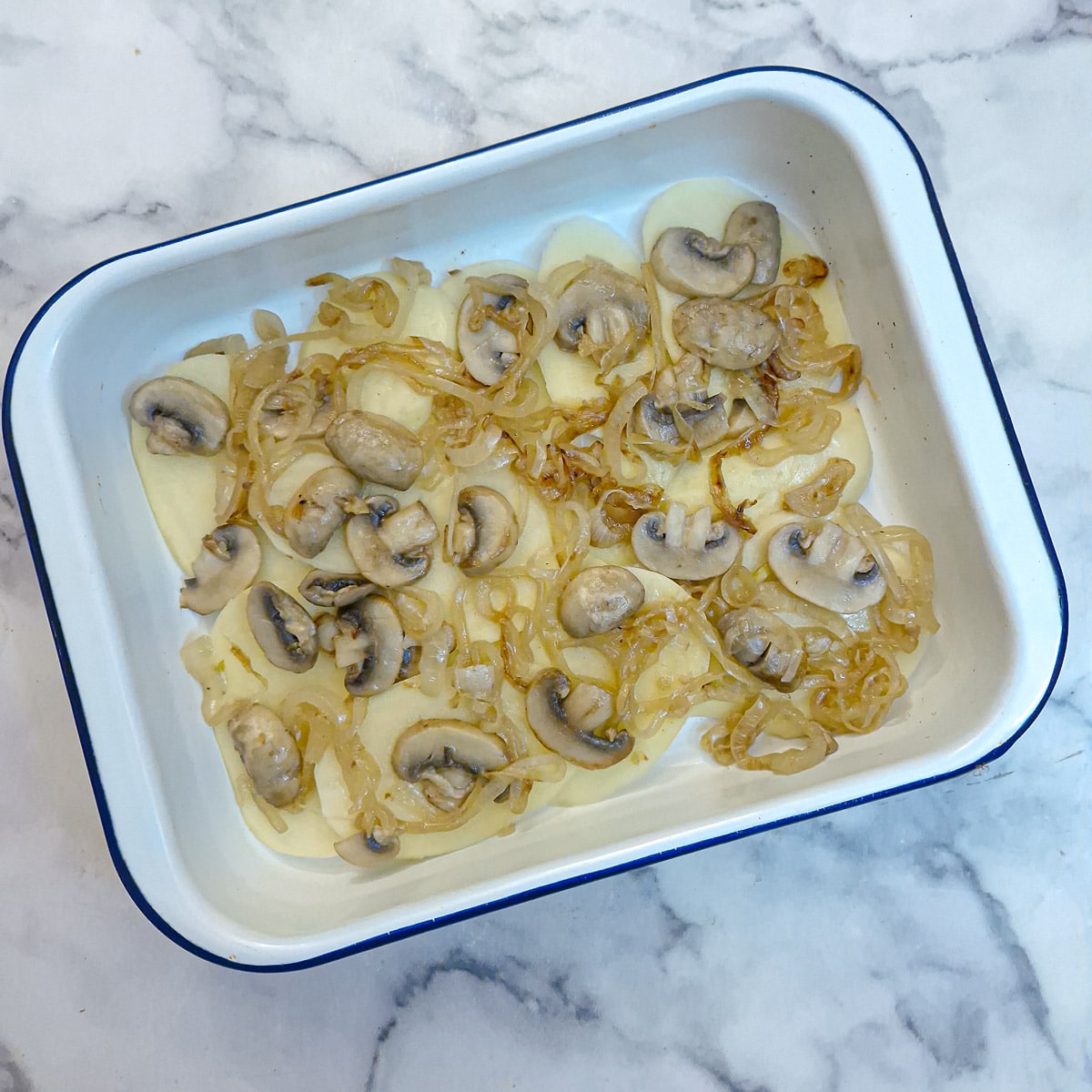 Step 3 - a layer of sliced potatoes in a baking dish topped with softened onions and mushrooms.