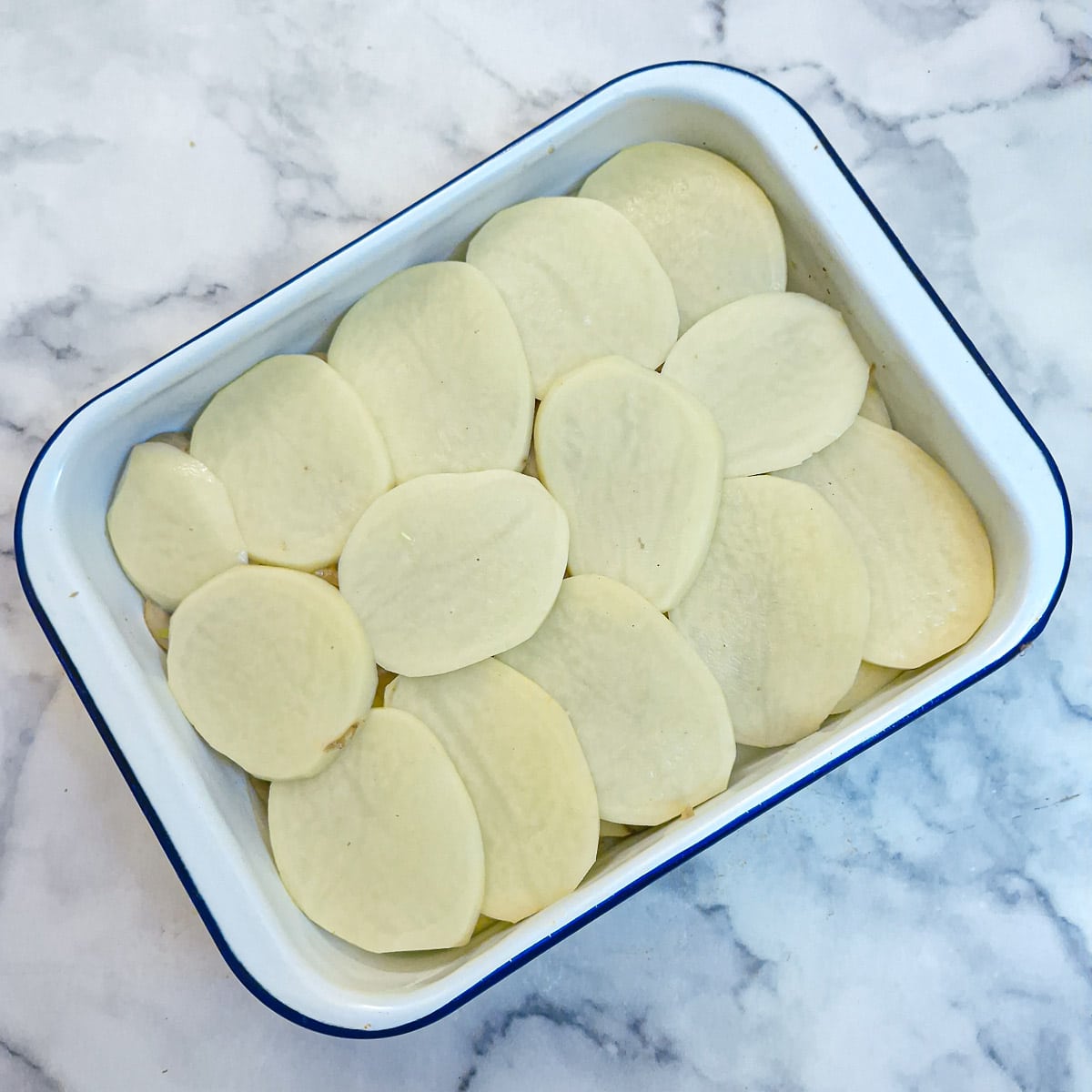 Step 4 - the layered potato bake in a dish, showing the final layer of sliced potatoes.