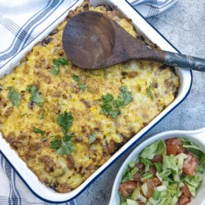 Overhead shot of a chilli con carne pasta bake in a white enamel dish with a green salad on the side.