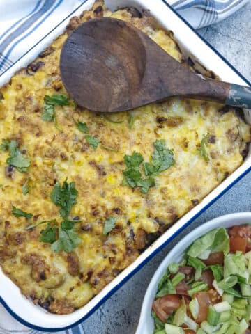 Overhead shot of a chilli con carne pasta bake in a white enamel dish with a green salad on the side.