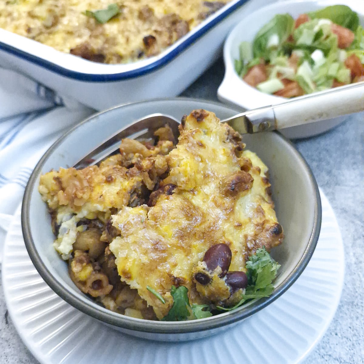 A helping of chilli con carne pasta bake in a white bowl on the table.