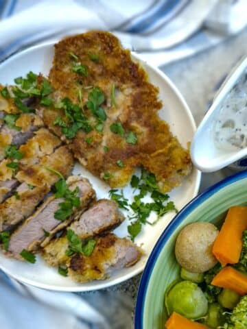 Crumbed pork chops on a plate, garnished with parsley. There is a jug of mushroom mustard sauce alongside.