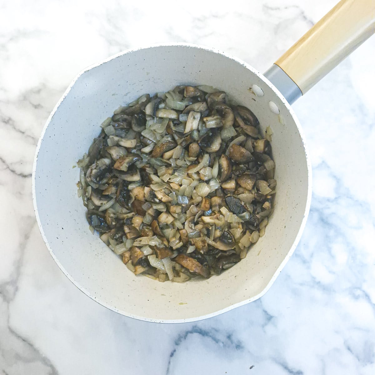 Softened onions and mushrooms in a saucepan.