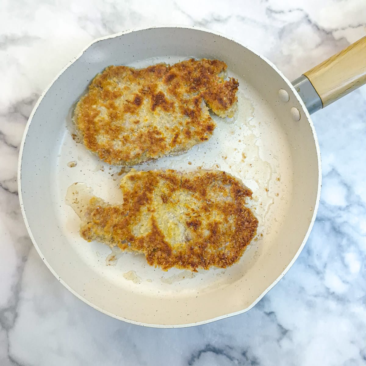 2 crumbed pork chops browning in a frying pan.