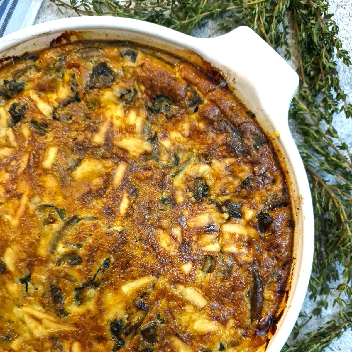 Overhead shot of a crustless mushroom, cheese and spinach quiche with springs of thyme on the side.