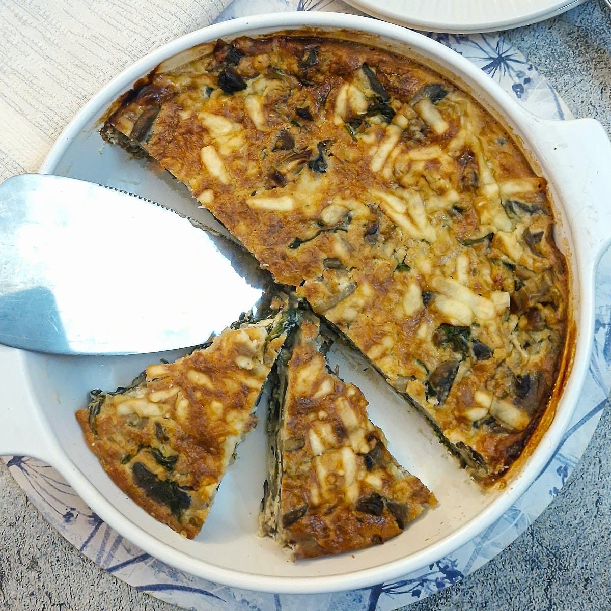 A crustless quiche in a white baking dish with some of the quiche cut into slices.