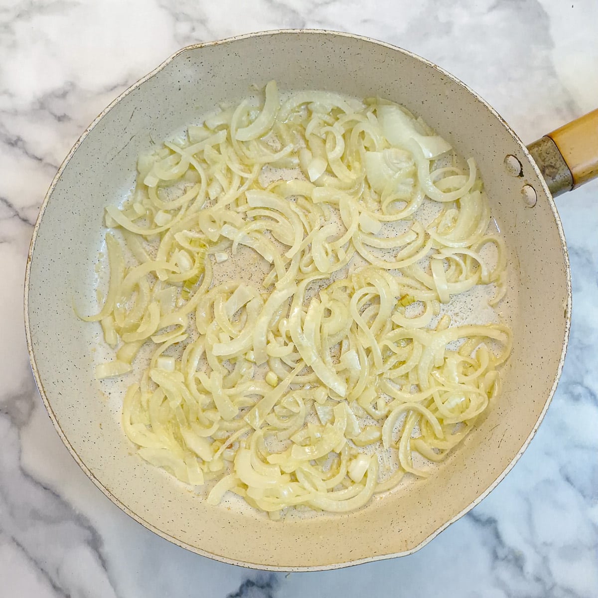 Sliced onions softening in a frying pan.