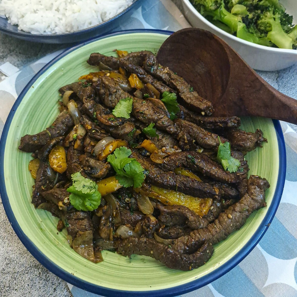 Cumin beef stir-fry in a green dish with a wooden serving spoon.