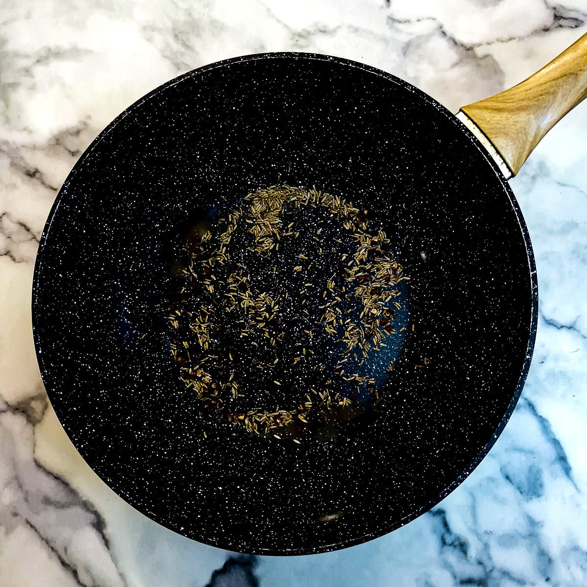Szechuan peppercorns and cumin seeds being toasted in a wok.