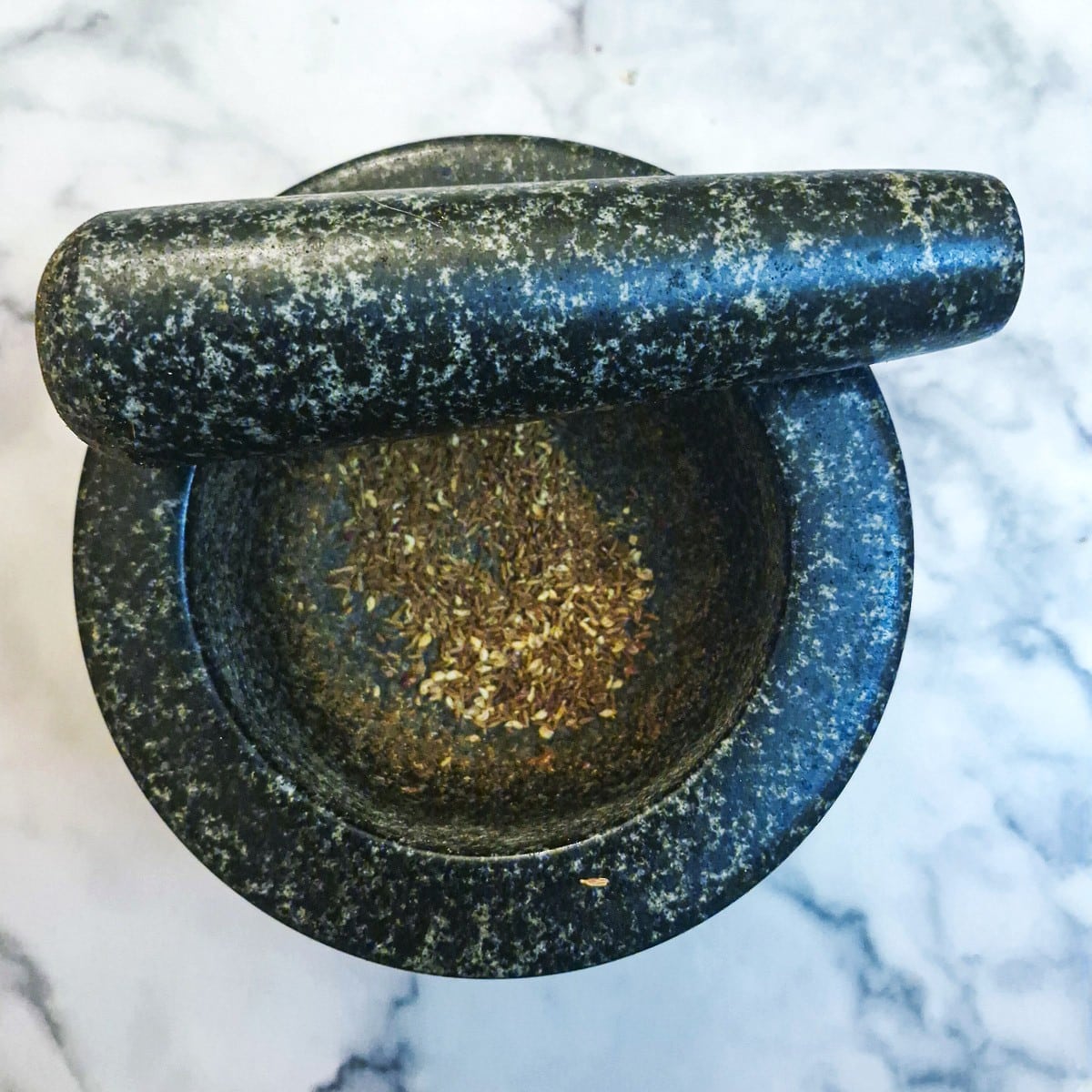 The toasted spices being ground in a mortar and pestle.