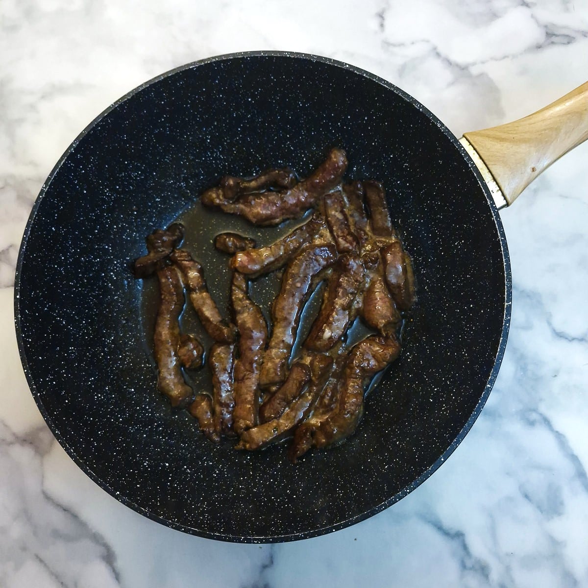 Marinated steak strips being seared in a wok.